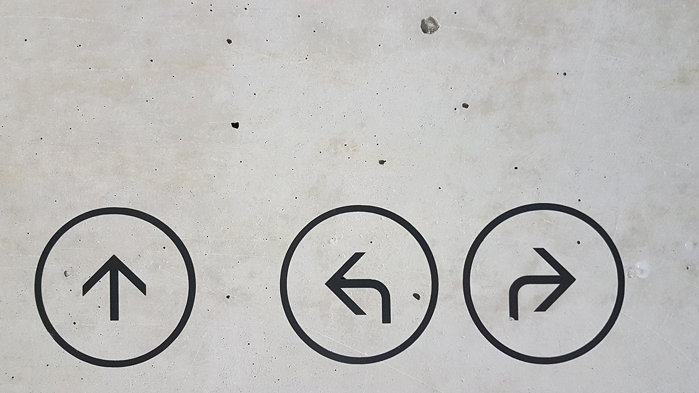 direction arrows enclosed in circles on a grey concrete wall